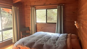 Une pièce en bois avec un lit, une chaise et une fenêtre avec des rideaux.
