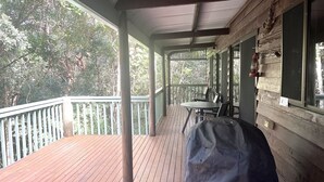 Une terrasse en bois avec une table et des chaises, un porche couvert et une vue sur les arbres.