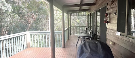 A wooden deck with a table and chairs, a covered porch, and a view of trees.