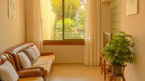A living room with a sofa, a potted plant, and a window with curtains. - House with large patio/solarium near the beach, in the center. (Malgrat de Mar)
