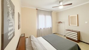 A bedroom with a bed, a ceiling fan, a wardrobe, a mirror, and a window with curtains. - House with large patio/solarium near the beach, in the center. (Malgrat de Mar)