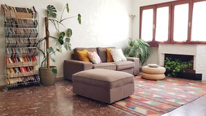 A living room with a sofa, ottoman, and a bookshelf filled with books. - Large and quiet apartment 20 minutes from Venice (Venezia)