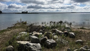 Vista de un lago con grandes rocas al frente y una orilla lejana con árboles.