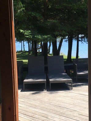 An outdoor seating area with wicker chairs and a wooden deck, overlooking a body of water and trees. - Beautiful Upper Peninsula Cottage (Hessel)