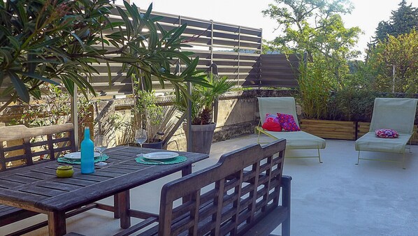 An outdoor patio with a wooden table set for dining, two lounge chairs, and a potted plant. - Apartment in the heart of the village • 50 m² terrace (Saint-Paul-Trois-Châteaux)