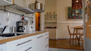 Cocina compacta con estufa, cafetera y comedor con mesa y sillas de madera.