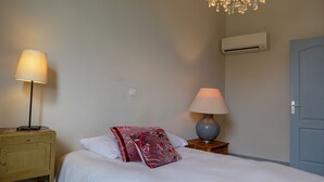 Un dormitorio con una cama, dos mesitas de noche, una lámpara, aire acondicionado y una puerta.