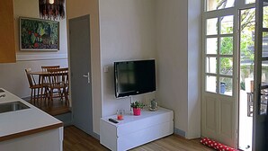 Un espacio habitable compacto con kitchenette, comedor, televisor montado y puerta que da a un balcón.