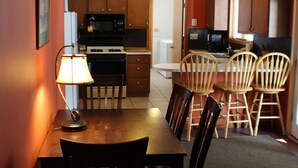 A compact kitchen with wooden cabinets, a microwave, and a stove. There is a dining table with chairs and a lamp. - 6 Bedroom Cottage Retreat with Conneaut Creek access (Kingsville)