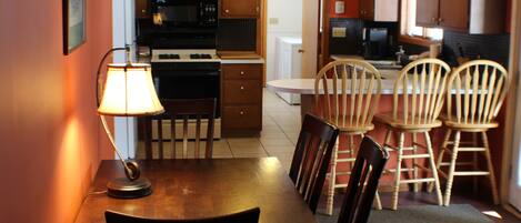 A compact kitchen with wooden cabinets, a microwave, and a stove. There is a dining table with chairs and a lamp.