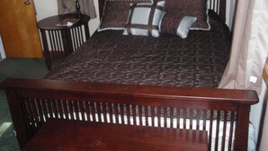 A neatly made bed with a dark patterned bedspread, two pillows, and a wooden headboard. - 6 Bedroom Cottage Retreat with Conneaut Creek access (Kingsville)