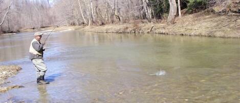 A person standing in a clear river, wearing a hat and fishing gear.
