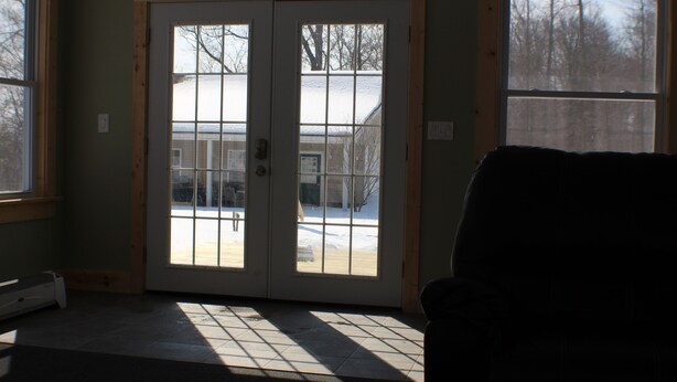 A room with a large sliding glass door leading to a snowy outdoor area, a black leather chair, and a heater on the floor. - 6 Bedroom Cottage Retreat with Conneaut Creek access (Kingsville)