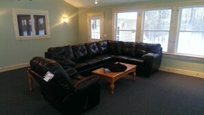 A living room with a black leather sectional sofa, a wooden coffee table, and a black leather recliner. - 6 Bedroom Cottage Retreat with Conneaut Creek access (Kingsville)