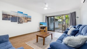 A living room with a sofa, coffee table, and a TV on a stand. There are three wall-mounted pictures, a ceiling fan, and a sliding glass door leading outside. - Cresta 1 Crescent Head (Crescent Head)