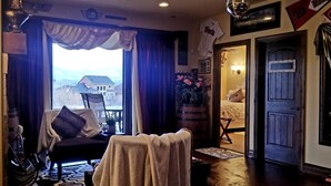 Ein gemütliches Zimmer mit Blick auf ein Haus und Berge, ein Esstisch mit Stühlen, eine Couch und ein kleiner Tisch mit einer Lampe.