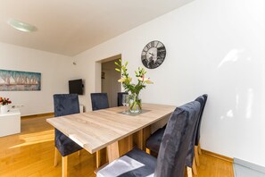 Un coin repas avec une table en bois, des chaises à revêtement sombre, un vase de fleurs et une horloge murale.