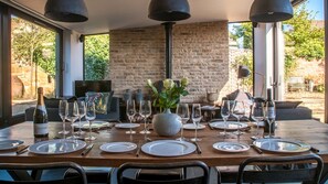 A dining table set for six with wine glasses, plates, and cutlery, a vase with flowers, and a stone wall in the background. - Bentleys - Three Bedroom Cottage, Sleeps 6 (Kingham)