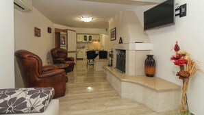 A living room with a fireplace, a TV mounted on the wall, and a dining area in the background.