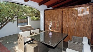 An outdoor patio with wicker furniture, a glass table, and a decorative vase.
