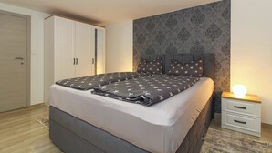 A bedroom with a bed, nightstands, a wardrobe, and a patterned wall.