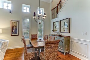 A dining room with a wooden table, wicker chairs, a chandelier, and framed artwork on the walls.