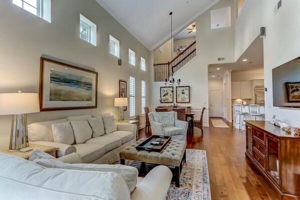 A spacious living room with a high ceiling, a staircase leading to an upper level, and a dining area with modern furniture.