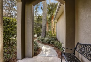 A covered walkway with a bench, surrounded by greenery and palm trees.