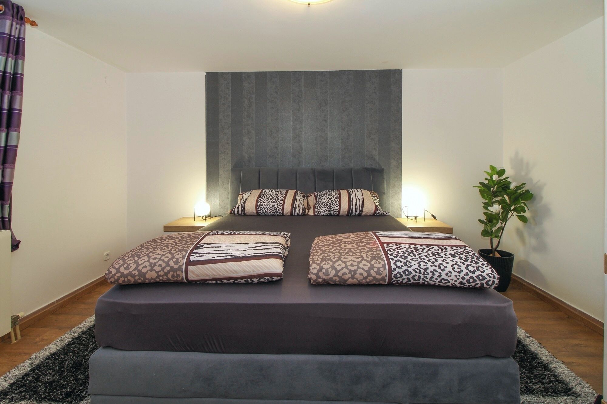 A neatly arranged bedroom with a large bed, two bedside tables, a headboard, and a potted plant.