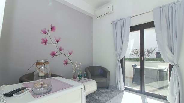 Une chambre moderne avec un bureau blanc, une chaise, un vase en verre avec des fleurs et une vue à travers une porte vitrée.