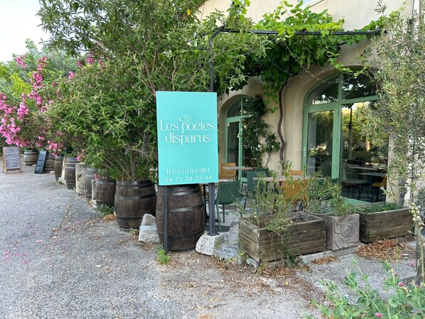 A restaurant sign, outdoor seating, and potted plants.