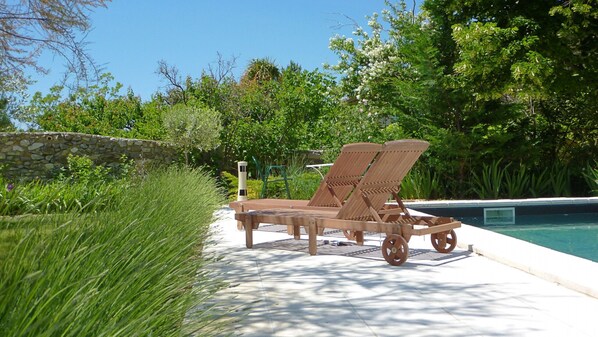 Un espace aménagé au bord de la piscine, avec deux chaises longues en bois et un mur en pierre.