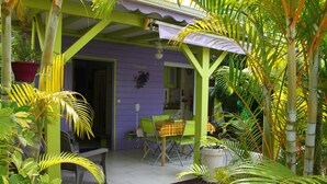 A covered outdoor seating area with a table and chairs, surrounded by potted plants and a bamboo structure. - Coco Bungalows. Bungalows 2 / pers sea at 100m (Ste Rose)