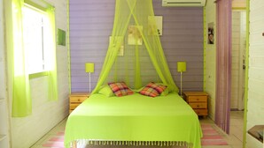 A room with a bed, bedside tables, a window with curtains, a wall-mounted air conditioner, and a door. - Coco Bungalows. Bungalows 2 / pers sea at 100m (Ste Rose)