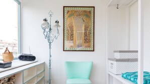 Ein Zimmer mit Holzboden, weißer Wand, einem Türkis-Stuhl, einer weißen Regaleinheit und einem gerahmten Bild.