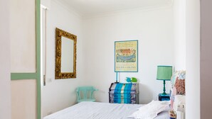 Ein Schlafzimmer mit einem Bett, einem Schminktisch, einem Sessel, einer Lampe und einem gerahmten Bild an der Wand.