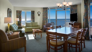 Habitación de hotel con comedor, sofá, televisor y vista al océano.
