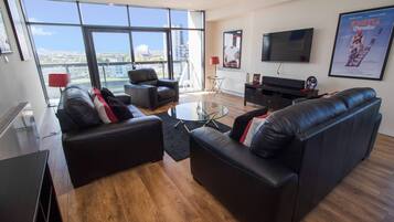 A modern living room with a large window, a flat-screen TV, and a leather sofa.
