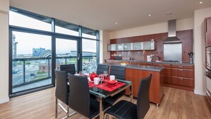 A modern kitchen with a large island, wooden cabinets, and a view of a cityscape through large windows. - Lancefield Quay - SECC & Hydro Arena, parking available (Glasgow)