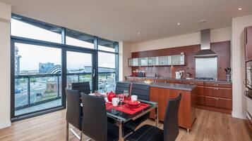 A modern kitchen with a large island, wooden cabinets, and a view of a cityscape through large windows.