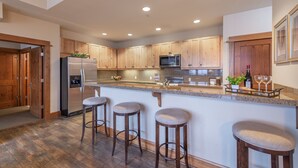 A spacious kitchen with wooden cabinets, a stainless steel refrigerator, a microwave, and a bar area with stools. - Iron Horse North - Luxury in the Northstar Village! (Truckee)