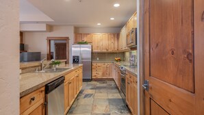 A modern kitchen with wooden cabinets, granite countertops, stainless steel appliances, and a tiled floor. - Iron Horse North - Luxury in the Northstar Village! (Truckee)