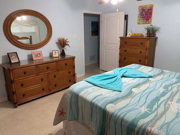 A bedroom with a bed, dresser, mirror, and a door leading to another room.
