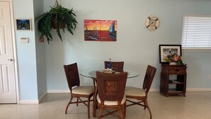 Un coin repas avec une table ronde en verre, entourée de chaises en osier, d’une plante en pot et d’œuvres d’art murales.
