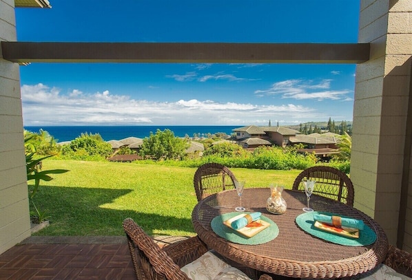 A patio with wicker furniture, a glass table, and a view of the ocean.