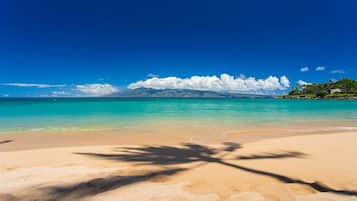 Une plage avec une eau turquoise et limpide, un rivage sablonneux et une montagne en arrière-plan.