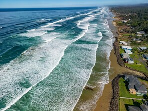 Vista aérea de uma área costeira com linha de costa rochosa, casas e uma visão clara das ondas do oceano.