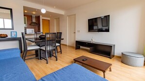 Ett modernt vardagsrum med en soffa, ett soffbord, en tv och en matplats med stolar och ett bord.