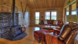 Een knus interieur van een chalet met een stenen open haard, houten wanden, een leren fauteuil en een bank.