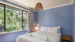 Ein Schlafzimmer mit einem großen Bett, zwei Kissen, einem Nachttisch, einer Lampe und einem Fenster mit Vorhängen.